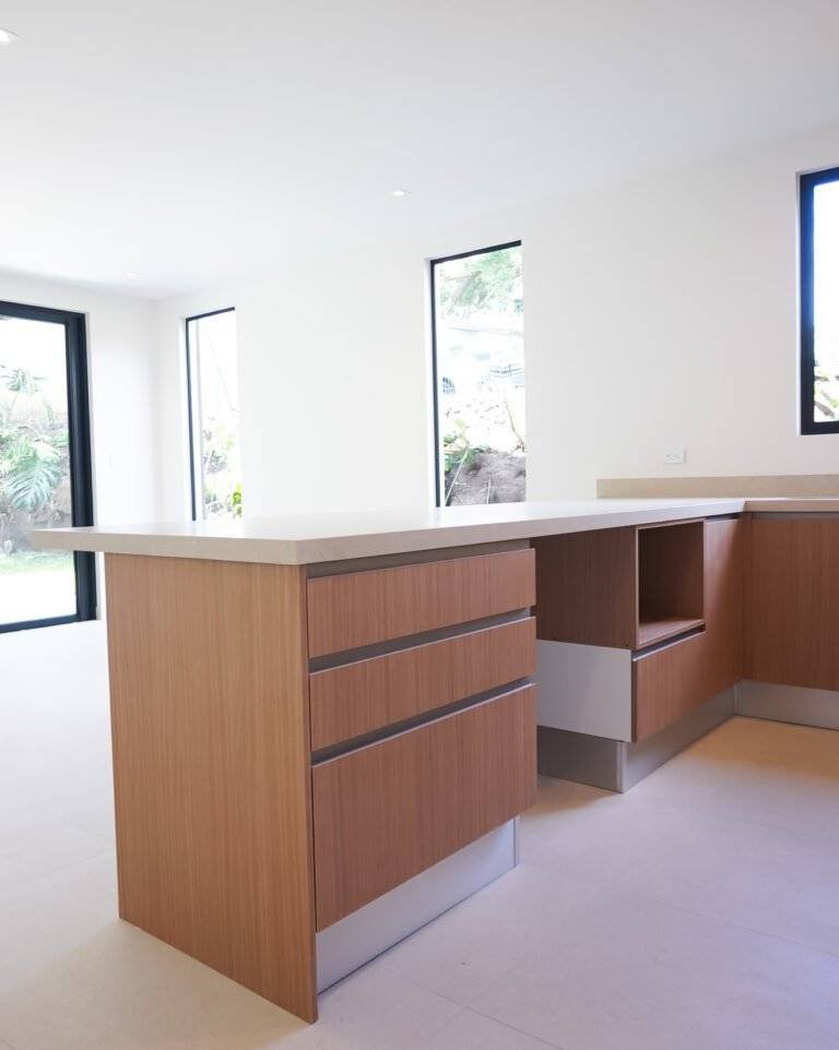 Cocina moderna con isla en L, sobres blancos y muebles de madera en casa en Barreal de Heredia (385 Francosta).